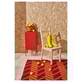 Red IVAR cabinet and wooden chair with yellow rain boots and lemons on herringbone orange-red rug.