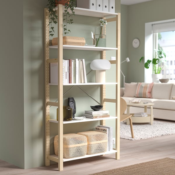 IVAR pine bookshelf near green wall, holding books, vases, baskets. Airy, functional design.