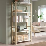 IVAR pine bookshelf near green wall, holding books, vases, baskets. Airy, functional design.
