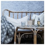 A cozy outdoor setting with a wicker chair, gray polka dot blanket, table with blue candle, glasses, and a bottle. Snowy background.