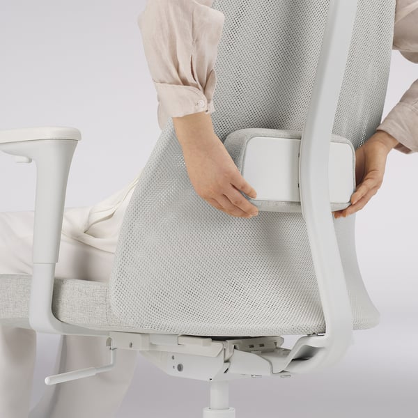 Adjusting lumbar support on ergonomic office chair. Woman securing lumbar support under mesh back.