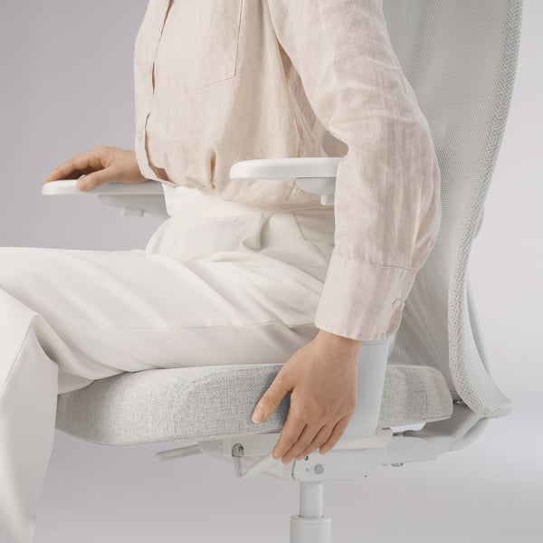 Person sitting on a white ergonomic office chair, adjusting seat height.