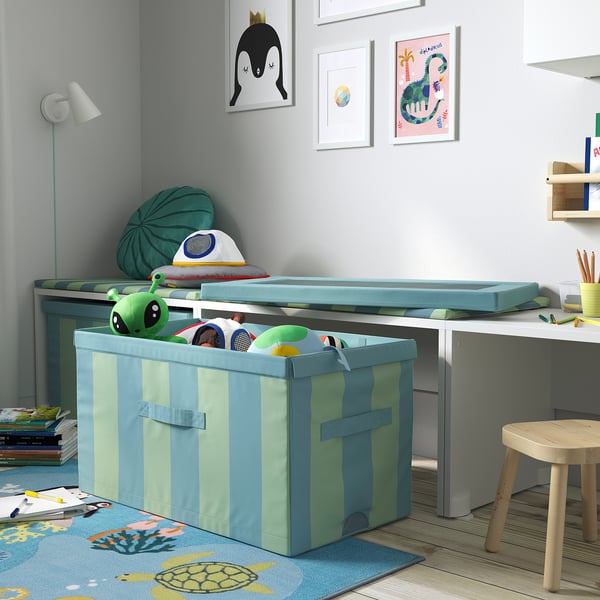 Playroom with blue-green striped toy box, toys, and wall art. Organizes with partitions. Ages 3+.