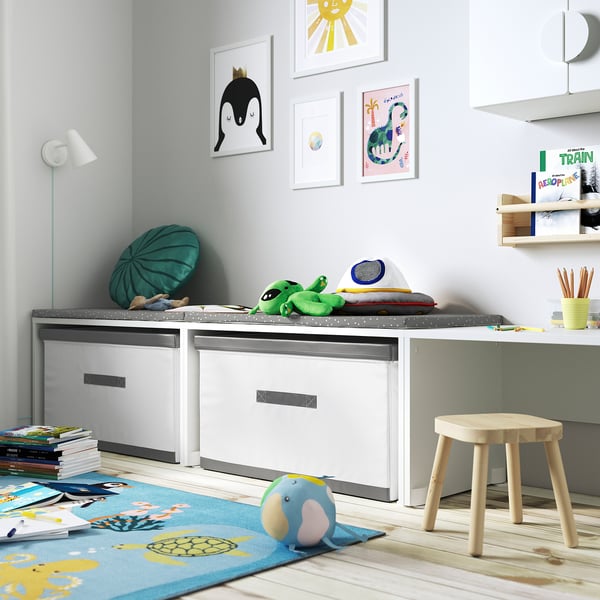 Kids room with toys, blue rug, art. Cabinet with green cushion, blue parrot. Bright & lively.