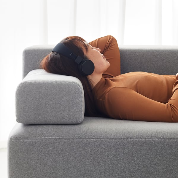 A person listens to headphones on a gray JÄTTEBO sofa with brown cushions.