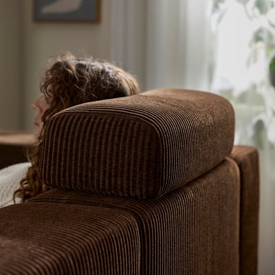 A person rests their head on a brown, striped JÄTTEBO modular sofa cushion, showcasing its use as a comfortable headrest.