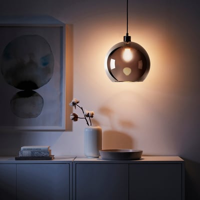 Copper JAKOBSBYN lampshade illuminates a vase with cotton branches on a sideboard, enhancing room decor.