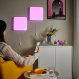Person adjusts smart light panel colors via phone in cozy room.