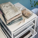 Folded clothes on a white JONAXEL mesh shelf, with a container of wooden clothespins.