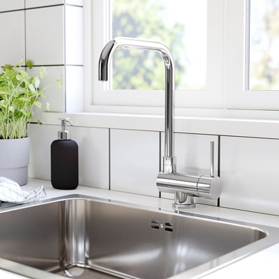 Modern kitchen sink with chrome faucet, black soap dispenser, and a green plant.