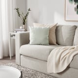 Minimalist living room with grey sofa, KÄRLEKSGRÄS cushions, side table with flowers, and light rug.