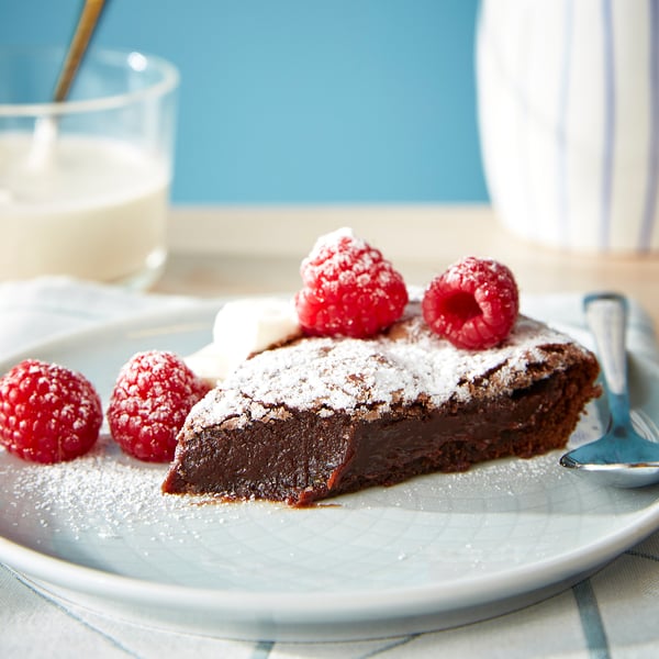 A chocolate cake with raspberries and powdered sugar on a blue plate.