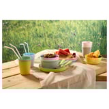 Table set with colorful plastic cups, bowls, and spoons, perfect for children. Food like fruit is present.