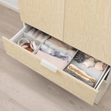Open wooden drawer with folded socks, scarves, and hat folded neatly in compartments.