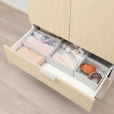 Wooden drawer organizer with compartments holding folded clothes and accessories in a neat, structured manner.