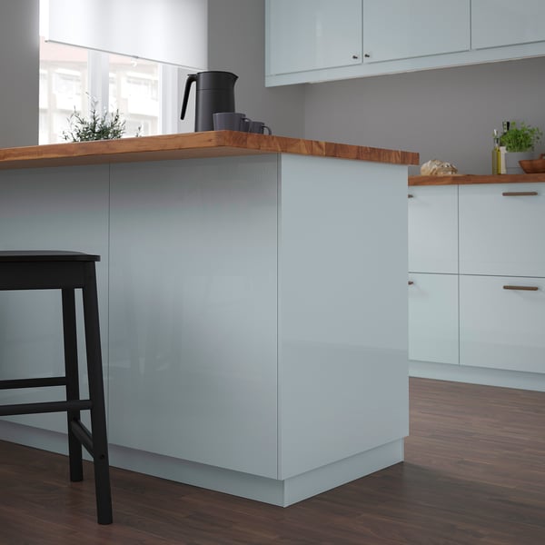 Modern kitchen with grey-blue glossy cover panel, black stools, wood countertop, and white cabinets.