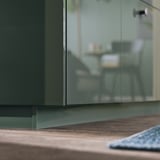 Modern kitchen with glossy green cabinet & wooden countertop.