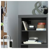 Modern grey shelf unit organized with books, boxes, and a lamp. Wood and metal design with grey finish.