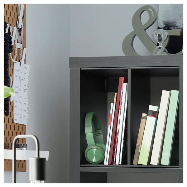 Dark grey KALLAX bookshelf with green headphones, books, and decor objects. Pegboard on left with notes and items.