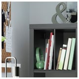 Dark grey KALLAX bookshelf with green headphones, books, and decor objects. Pegboard on left with notes and items.