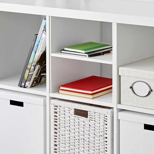 White KALLAX shelf unit with books, basket, and storage box. Books are neatly organized on shelves.