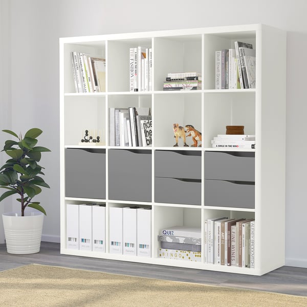 White KALLAX storage unit with shelves, books, games, and plant. Provides versatile storage for home.