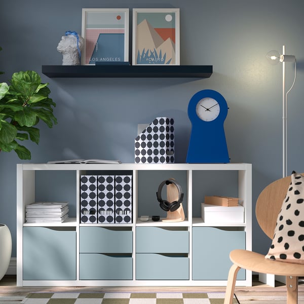 Modern living space with KALLAX storage, light blue drawers, polka dot box, blue clock, prints, plants.