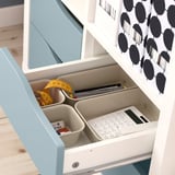 A KALLAX shelf with organized drawer inserts, holding office supplies including a calculator, pens, and measuring tape.