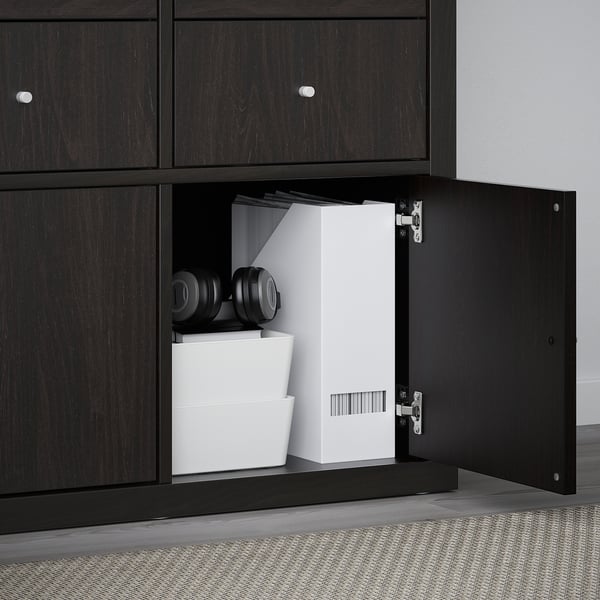 Black KALLAX shelf with door open, showing organized storage including white boxes and black headphones.