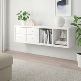 White ikea KALLAX shelves hold books, plants, and decor, narrow with drawers, between wall decor and a sofa.