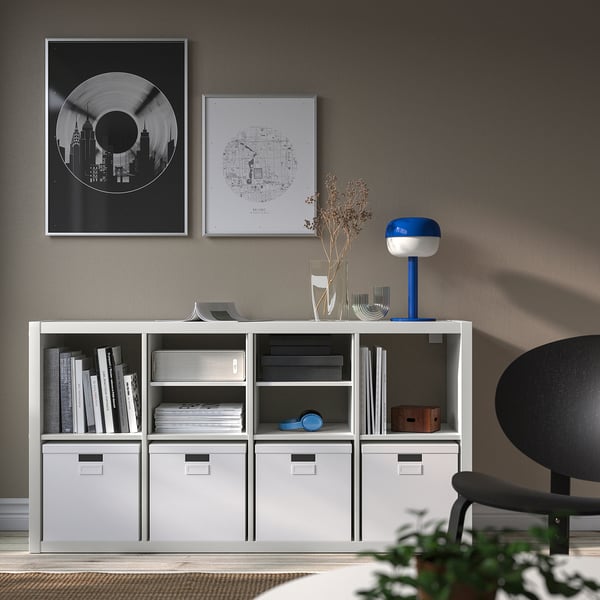 White KALLAX shelf with drawers, books, lamp and posters, black chair.