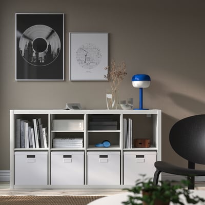 White KALLAX shelf with drawers, books, lamp and posters, black chair.
