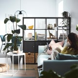 Cozy living room with KALLAX storage, lamp, blue couch, person reading.