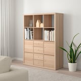 KALLAX shelf unit with books, decor, and plant. Beige sofa partially visible.