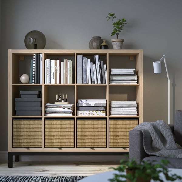 KALLAX shelving unit with books, decor, plants & storage boxes, grey armchair partial.