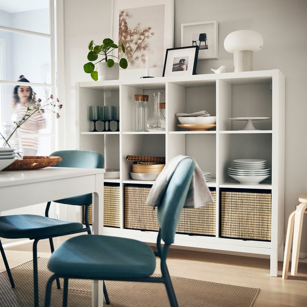 Modern dining area with white KALLAX shelving unit, blue chairs, and decorative items.