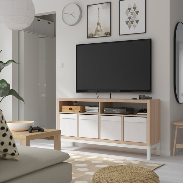 Minimalist tv room with KALLAX tv bench, flat-screen tv, gaming accessories, books, gray sofa, rug, wall art, clock, coffee table, and mirror.
