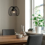 Modern dining setup with wooden table, dark chairs, KALLFRONT lamp, bowl, carafe, books, and plant.