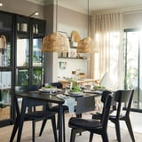 Modern dining area with KAPPELAND rattan pendant lamps, black cabinet, and large window.