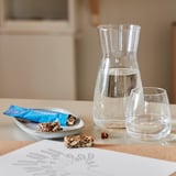 Glass carafe and glass with water, small plate with snack, menu on table.