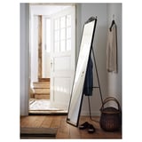 A KARMSUND mirror with hooks, placed on a wooden floor. The frame is black and the mirror is rectangular.