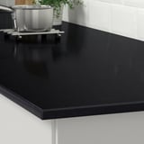 Black quartz countertop in kitchen, resistant to stains and scratches, with shiny surface and rounded edges.