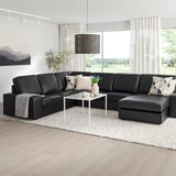 Elton black KIVIK sectional, leather & fabric blend, large & comfy, wide armrests, positioned before tall windows, complemented by white decor.