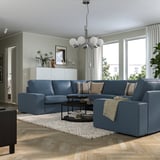 Modern living room with blue KIVIK sectional sofa, wooden floor, chandelier, and large windows with curtains.