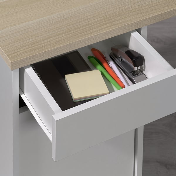 Open desk drawer showing stationery items: stapler, scissors, pens, sticky notes, and notepad.