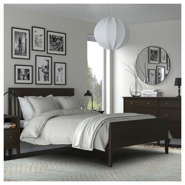 Modern bedroom with dark bed, white bedding, black-and-white photos, pendant light, mirror, and rug.