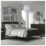 Modern bedroom with dark bed, white bedding, black-and-white photos, pendant light, mirror, and rug.