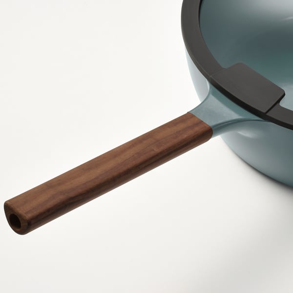 Close-up of a modern sauté pan handle. Dark brown wood, sleek design, attached to smooth, light blue pan.