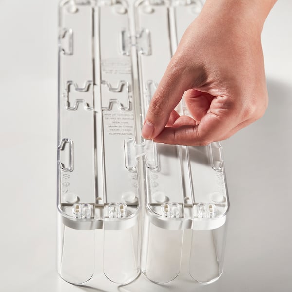 Hand holds clear plastic drink organizer, adjusting width for bottles, ensuring neat fridge storage.