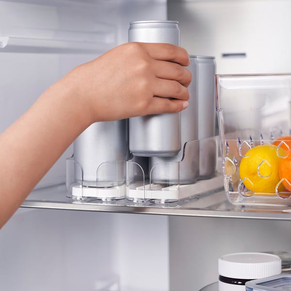 Person places can in fridge organizer. The holder adjusts to fit various drink sizes and automatically pushes items forward for easy access.